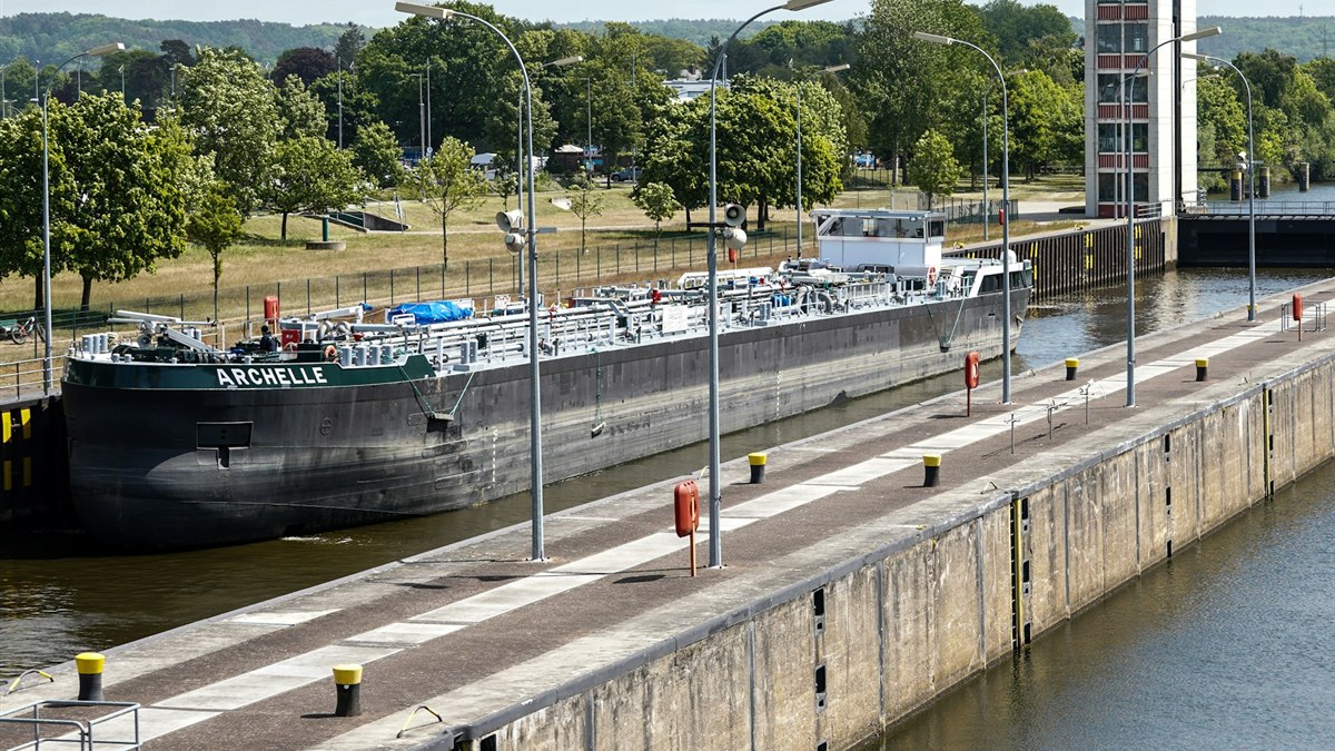 A large barge sitting inside a canal lock chamber, with an empty second lock alongside it and the tall lock towers and gates beyond.